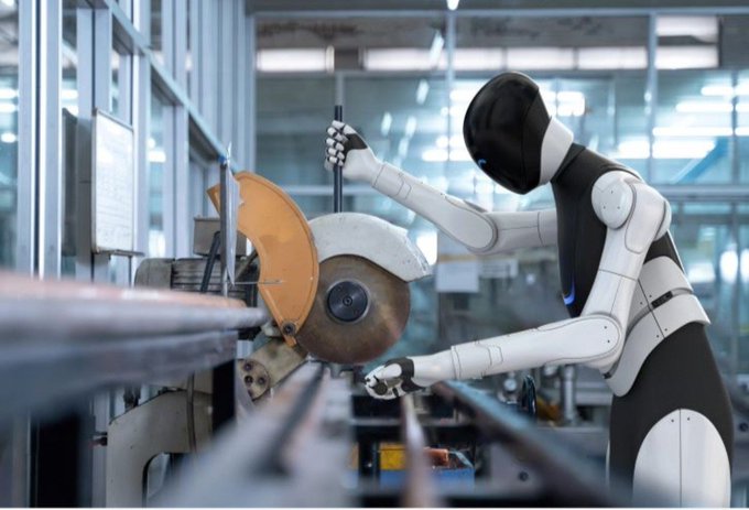 The image features a robot with white and black colors, standing next to a machine that has an orange blade. The robot appears to be engaged in some sort of activity or work related to the machine's operation. The background shows a factory setting where various machines are present, indicating that this scene takes place within a manufacturing environment.