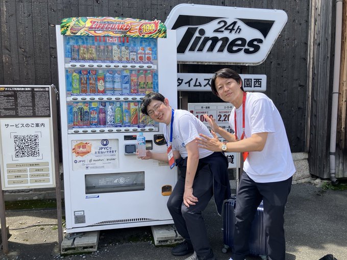 Two men pose next to a "Lifeguard 100" vending machine, which displays "JPYC" as an accepted payment method. The post describes their encounter with JPYC's Okabe-san on their way to inspect a JPYC vending machine.