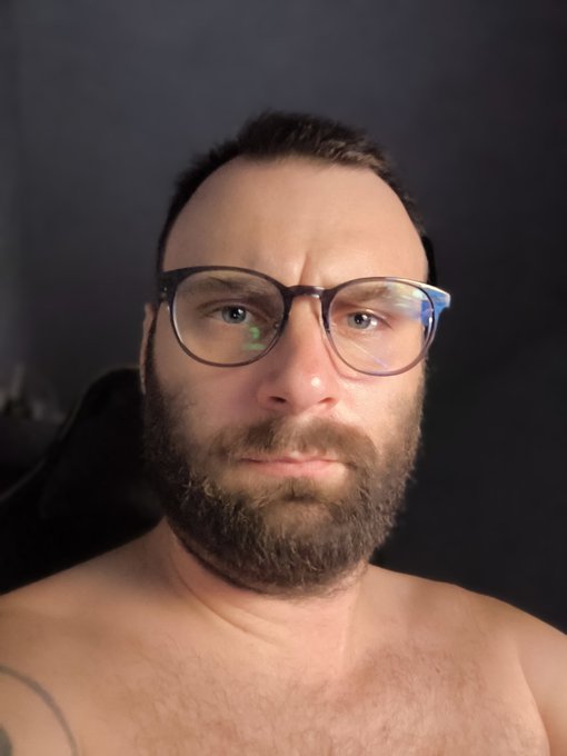 A bearded man with glasses takes a shirtless selfie against a dark background, likely as part of his daily selfie series tracking ZK token's price movement, with no visible text or price chart in the image itself to reflect the current 0% change mentioned in his post.