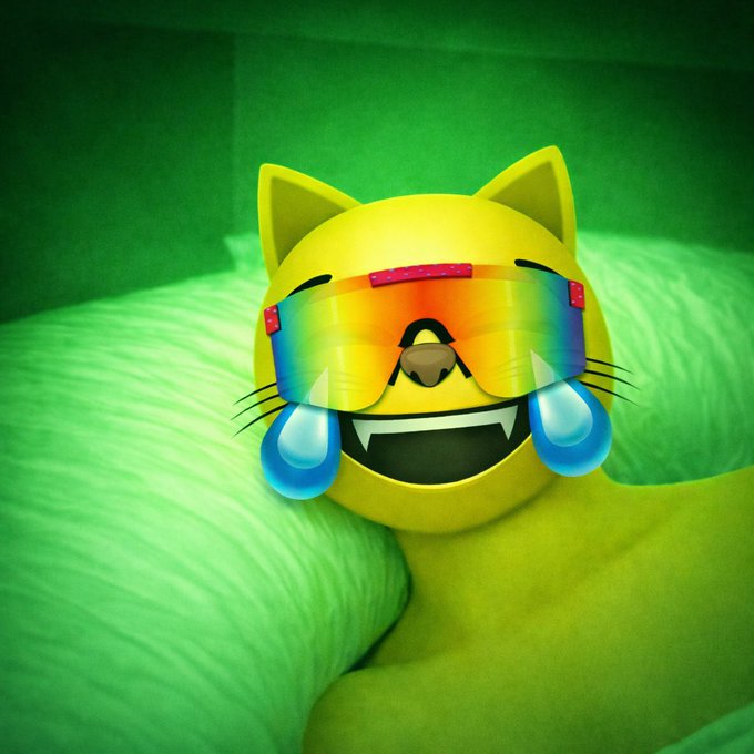 A bright yellow cat emoji wearing rainbow sunglasses beams with a toothy grin and cartoonish tears of joy, resting against a green pillow — capturing the euphoric, "something big is coming" energy of $MOG.