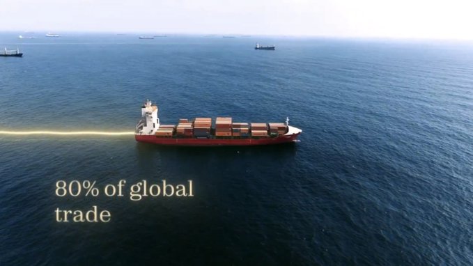 An aerial photograph of a red container ship at sea, with other cargo vessels in the background and the text '80% of global trade' displayed on the left side.