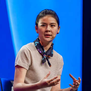 Bitget CEO Gracy Chen, wearing a dark patterned scarf and headset microphone, speaks on stage with an expressive gesture against a bright blue backdrop, visually accompanying the post's message about diverse Bitcoin strategies—where she awaits $50K while others buy now.
