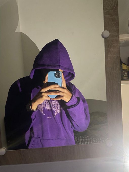 A mirror selfie of a person wearing a purple hoodie with the hood up, holding a blue smartphone in front of a mirror.