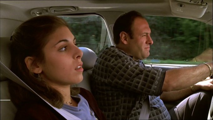 A scene from a movie showing a young woman with brown hair and a man in a checkered shirt sitting in a car.