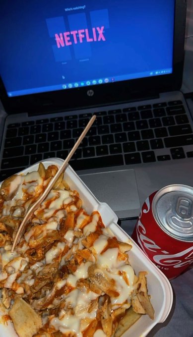 A container of loaded fries with cheese sauce and a Coca-Cola can sit on the keyboard of an HP laptop displaying the Netflix login screen, capturing a cozy nighttime streaming setup. The scene perfectly matches a "good night" message to friends, suggesting a relaxing evening of Netflix and comfort food.