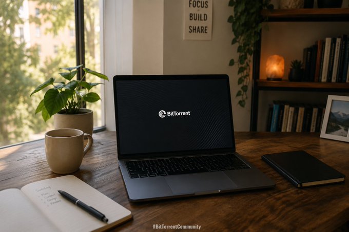 A laptop on a wooden desk displays the BitTorrent logo on its screen, accompanied by a coffee mug, notebook, plant, and bookshelf, with the hashtag '#BitTorrentCommunity' at the bottom.