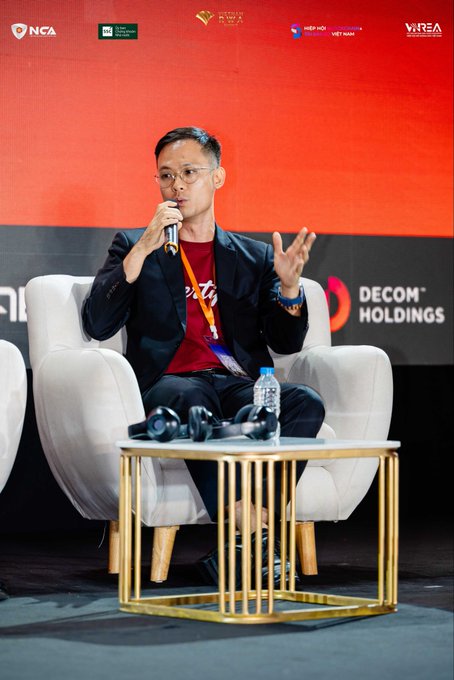John Kiew of CertiK speaks on a panel at the Vietnam RWA Summit, seated in a white chair with a microphone, against a backdrop featuring logos for "NCA," "RWA Summit," and "DECOM Holdings." The image reflects the post's mention of his participation in discussions on digital asset security and the transition from traditional markets to on-chain finance.