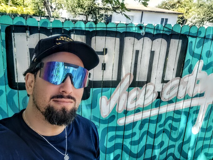 A man wearing a black cap and blue reflective sunglasses poses in front of a graffiti-style mural reading "Solana Miami," reflecting the post's themes of being a Solana enthusiast, gamer, and content creator who embraces the "bullish" lifestyle in the crypto space.