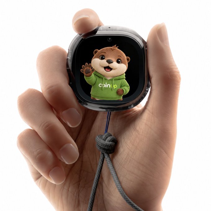 A hand holds a small smartwatch-like device displaying a cartoon otter mascot in a green 'coinup' hoodie waving at the viewer.