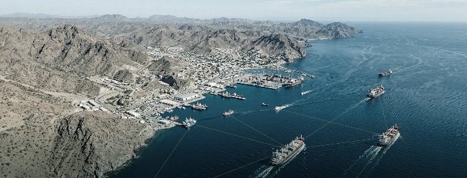 An aerial view of a coastal port with multiple cargo ships navigating the waters and docking at the harbor, illustrating the busy maritime activity that AIS systems like Sea Verity aim to track and verify.