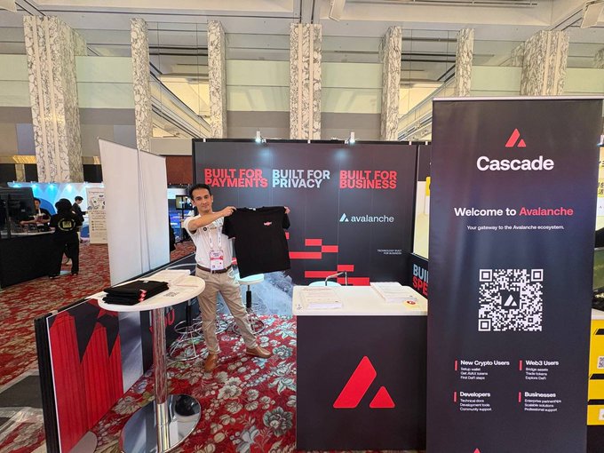 A smiling exhibitor stands at the Avalanche/cascade booth (G-47) at WebX, holding up a black t-shirt in front of banners reading "Built for Payments, Built for Privacy, Built for Business" and "Welcome to Avalanche" with a scannable QR code. The image directly illustrates the post's invitation for WebX attendees to visit the booth for ecosystem info and community engagement.
