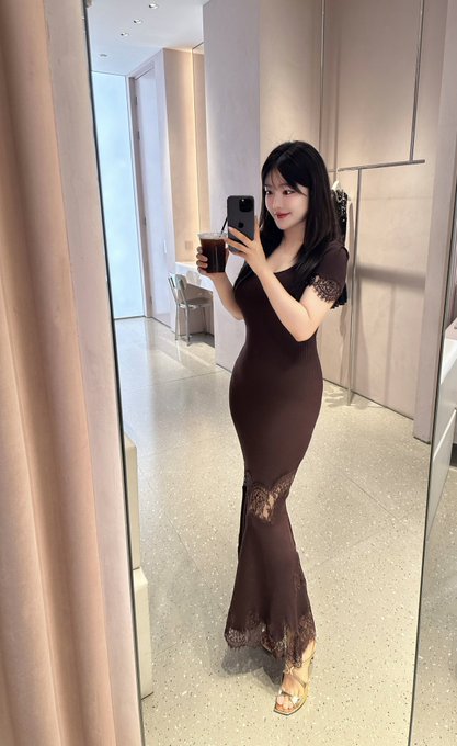 A woman in an elegant brown lace dress takes a mirror selfie while holding a drink, dressed in a refined outfit with strappy heels. The image complements the post's theme of enjoying the rewards of smart financial choices, showcasing a stylish lifestyle funded by crypto earnings.