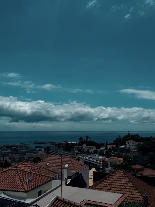 A scenic coastal town view featuring terracotta-roofed buildings overlooking a calm sea under a partly cloudy sky. The image does not contain any visible text, numbers, tickers, or names, and does not relate to the accompanying "GOOD MORNING / Reply with your SOL address" post.