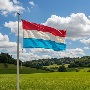 A flag with red, white, and blue horizontal stripes waves on a flagpole against a cloudy blue sky, set above a rolling green countryside.