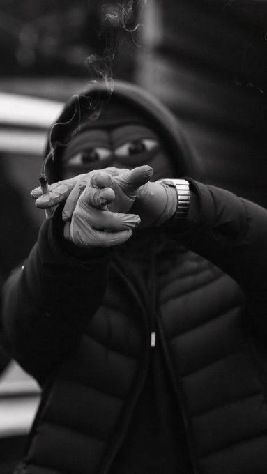 A hooded figure in a black puffer jacket exhales smoke through gloved fingers holding a cigarette, channeling a moody, cinematic vibe. The shadowy aesthetic reinforces the "$HPEPE / DO_IT_FOR_THE_HOOD" energy—urban, mysterious, and dripping with street-cool attitude.