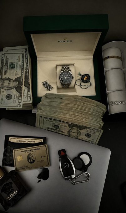 A flat lay showcasing symbols of financial success—including a Rolex watch in its green box, stacks of $50 bills, American Express Platinum cards, a Mercedes car key, rings, and a Versace cologne—visually reinforces the post's message about pursuing financial freedom through Web3 work and building one's reputation from scratch.