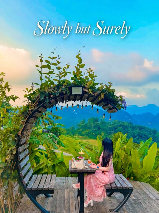 A scenic view of a woman in a pink dress sitting at a table under a circular vine-covered archway overlooking green mountains, with the text 'Slowly but Surely' overlaid at the top.