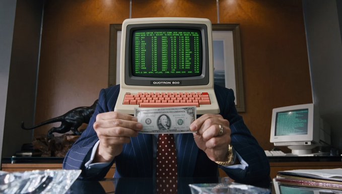 A surreal image of a person in a suit holding a US one-dollar bill, with a vintage computer monitor displaying 'ERROR' covering their head. The monitor has 'QUOTRON 500' printed on it.