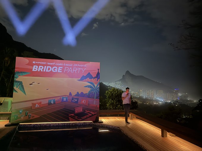 A speaker presents at a nighttime "BRIDGE PARTY" event with a backdrop displaying logos for Superteam, team, OGMI, REAP, and Aventis, set against Rio de Janeiro's illuminated skyline with Christ the Redeemer visible in the distance. The scenic mountaintop venue beautifully captures the appreciation expressed in "Thank you, Rio!"