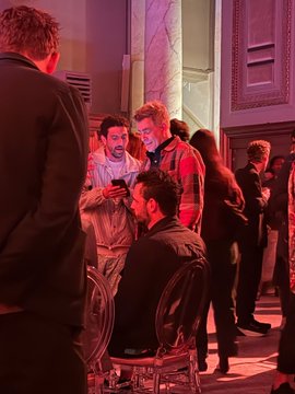 A group of people gather in a dimly lit room with red lighting, appearing to be at a social event or networking gathering.