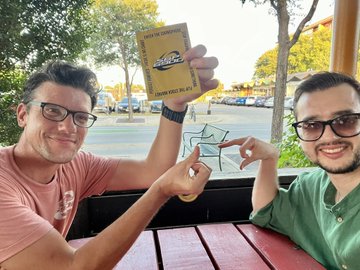 Two men smiling outdoors while holding a Sep card and a small drawing of a horse.