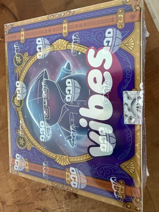 A sealed box of "Wibes" trading cards, specifically the "Legend of the Lils" series 2, rests on a wooden surface. The purple and gold packaging features a stylized character design with "Wibes" prominently displayed, tying into the post's excitement over new collectible card series.