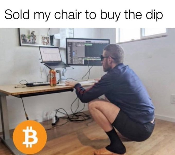 A meme image with the caption 'Sold my chair to buy the dip' showing a man squatting at a desk using dual monitors, with a Bitcoin logo in the corner.