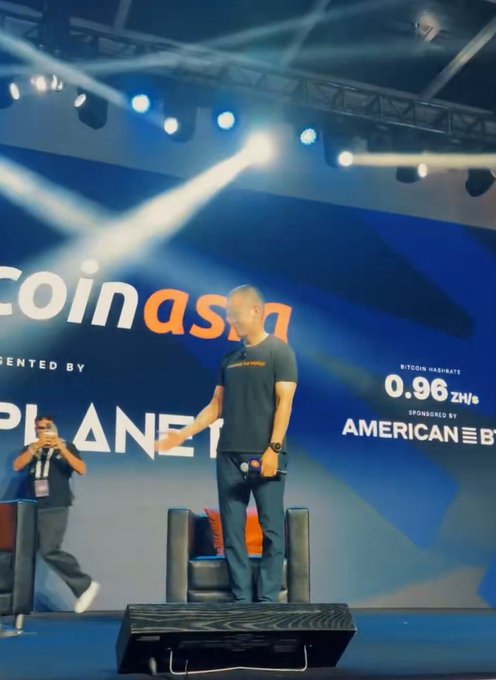 A man stands on a stage at a 'Coin Asia' event presented by 'PIANETA', with a Bitcoin hashrate of '0.96 ZH/s' and sponsor 'AMERICAN' visible on the backdrop.