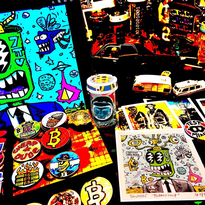 A colorful display of crypto-themed merchandise, including prints, pins with Bitcoin logos, and a silver coin with '1000101001' engraved on it.
