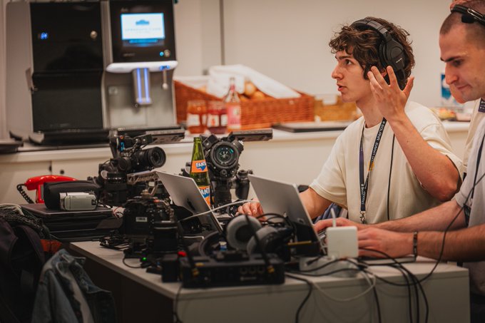 A behind-the-scenes shot at Solana Summit Germany shows crew members wearing headsets and operating multiple professional cameras and laptops to produce event coverage, with a beverage dispenser and refreshments visible in the background. The image captures the fast-paced content creation process described in the post, highlighting the teamwork that made the timely coverage possible.