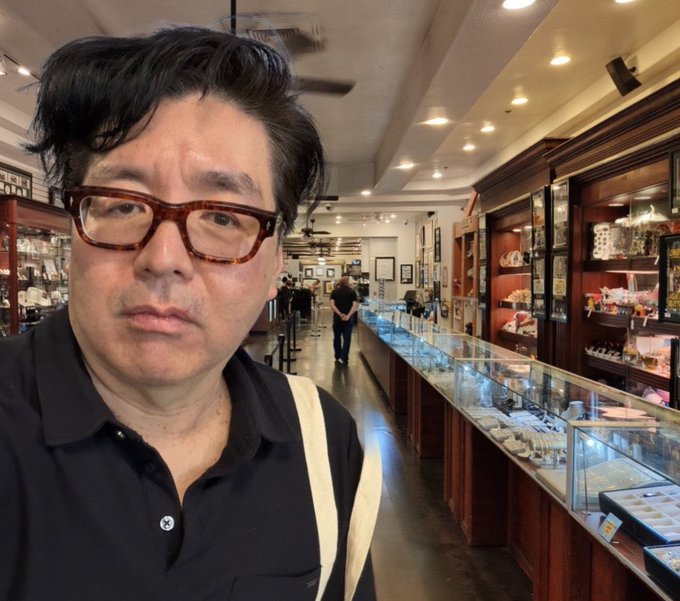 The image features a man wearing glasses standing inside an antique store, surrounded by various items such as jewelry and antiques displayed behind glass cases. The man appears to be posing for a picture while looking at the camera with a serious expression on his face. In the background, there are other people present in the store, adding to the atmosphere of the scene.

The post that reads "I’m looking to pawn some Ethereum." is likely related to the antique store or the man's personal situation. It could be an advertisement for a cryptocurrency exchange service, suggesting that the man might be interested in trading Etherium or considering selling his items at the store.