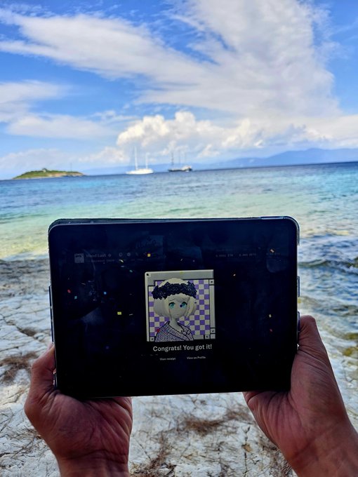 Hands holding a tablet displaying an NFT of an anime-style character with the text 'Congrats! You got it!' against a beach backdrop with sailboats and mountains.