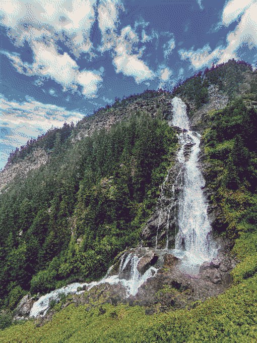 A scenic landscape photograph shows a tall cascading waterfall flowing down a rocky mountainside covered in lush green trees, set against a vivid blue sky with scattered white clouds.