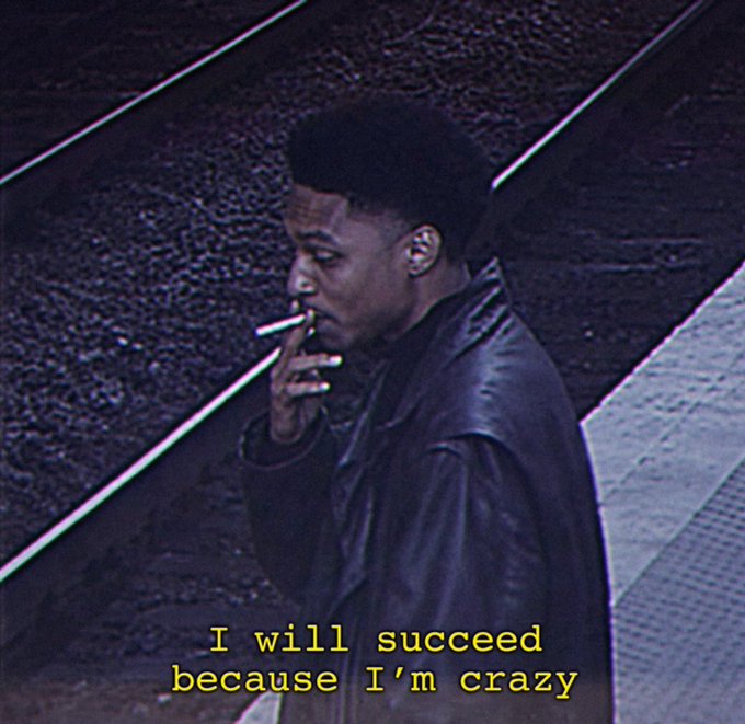A Black man smoking a cigarette on what appears to be train tracks, with yellow text overlay reading 'I will succeed because I'm crazy'.
