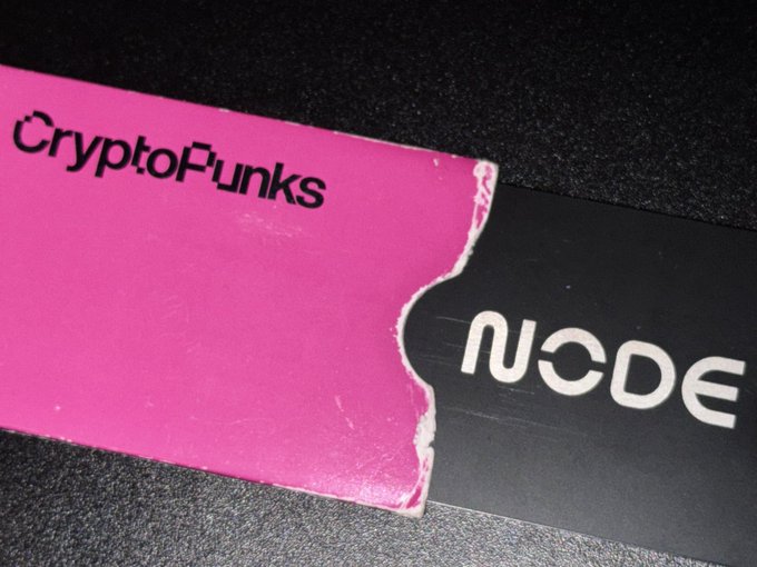 A torn pink sticker with 'CryptoPunks' partially peeled away from a black surface displaying the white text 'NODE'.