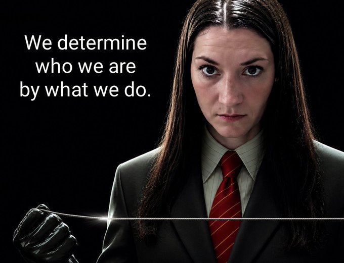 A woman in a dark suit and red tie holds a thin wire across the frame with a black-gloved hand, accompanied by the text "We determine who we are by what we do."
