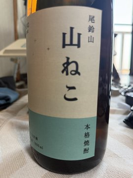 The image features a bottle of wine with Japanese writing on its label, which reads "おはようございますよく寝た今朝はランオフ、今週はから逃れらない週でする山ねこのソーダ割美味しい', 'LSD', and 'DURABILITY'. The bottle is placed on a table, with the background blurred.