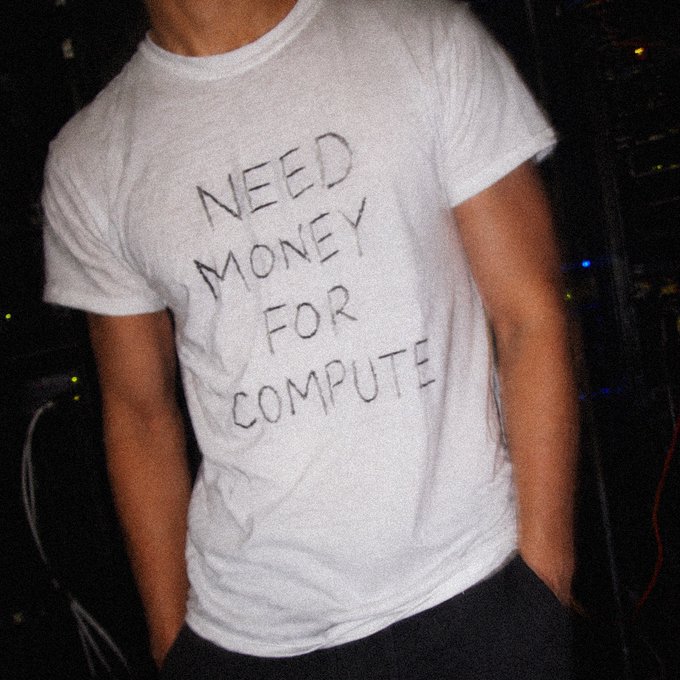 A person wearing a white t-shirt with the handwritten-style text 'NEED MONEY FOR COMPUTE' stands in a dimly lit setting.