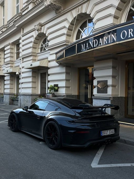 A black Porsche 911 GT3 is parked on a city street in front of an elegant building with a sign reading 'MANDARIN OR'.
