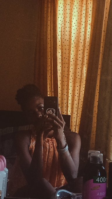 A dimly lit selfie of a person holding up a phone with an Apple logo sticker in front of their face, with a curtain and a bottle labeled 'ABO 400' in the background.
