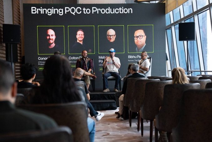 Three men sit on a stage in front of an audience during a panel discussion titled 'Bringing PQC to Production,' featuring headshots of speakers Conor, Colton, Meh, and Bibhu.