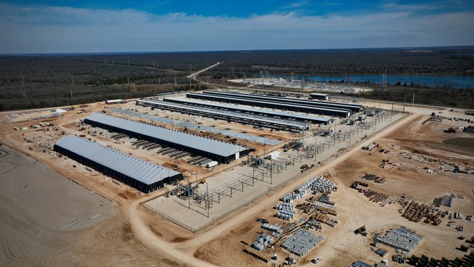 An aerial view of a large industrial construction site with multiple long warehouse-style buildings under development in a flat, open landscape.