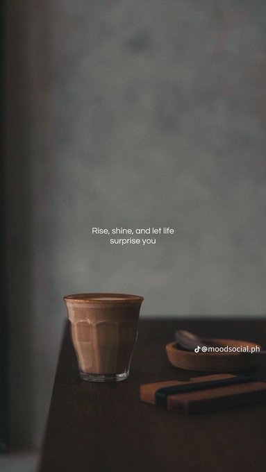 A moody still life photograph featuring a glass cup of coffee and small cookies on a dark table, with the text 'Rise, shine, and let life surprise you' overlaid and a TikTok watermark '@moodsocial.ph'.