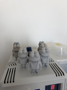 The image shows a collection of small figurines, including frog statues, sitting on top of an air conditioning unit or fan. The figurines are arranged in various positions, with some standing upright while others sit down. The scene appears to be set up for display or storage purposes, as the figurines are placed near a white wall and a shelf. The post about GM! Work for $PEPE physical boxes is related to this image because it suggests that these frog statues might be part of an ongoing project involving the creation of physical boxes using foam material.