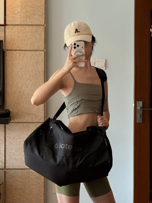 A mirror selfie showing a woman in athletic wear and a beige cap holding a phone, while carrying a black duffel bag with "Gate VIP" printed on it—highlighting the brand sponsorship for her fitness and Olympic training prep mentioned in the post.