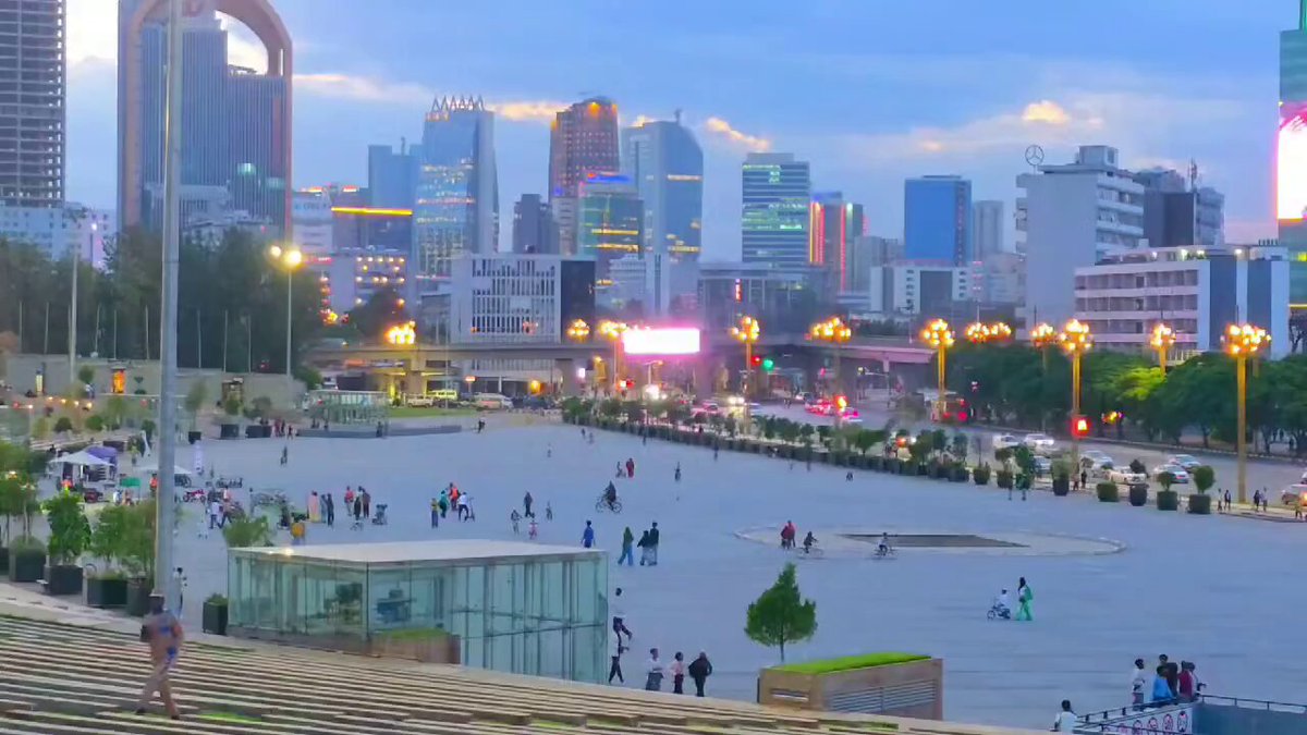 The image shows a cityscape with tall buildings, including one that has the number "IOTA" written on it. There are many people walking around outside of these buildings, creating a lively atmosphere. The photo appears to be taken from an elevated perspective, providing a bird's eye view of the city and its inhabitants.
