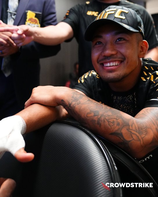 UFC fighter Maxim Grishin smiles broadly while seated in a UFC-branded setting, with "UFC" visible on his black cap and shirt, aligning with the post promoting UFC 331 on Paramount Plus and sponsored by CrowdStrike (whose logo appears at the bottom).