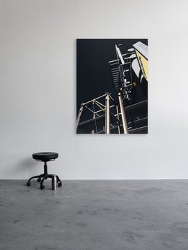 A gallery space displays a large photograph of a traffic signal structure against a dark sky on a white wall, with a small black stool positioned on the polished concrete floor.