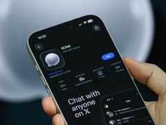 A hand holds a smartphone displaying an AI chat interface with the text 'Chat with anyone on X', advertising an AI companion app called Nomi.