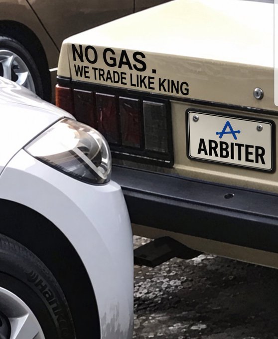 The rear of a beige vintage car features a decal reading 'NO GAS . WE TRADE LIKE KING' above a license plate displaying 'ARBITER' with a stylized blue 'A'.
